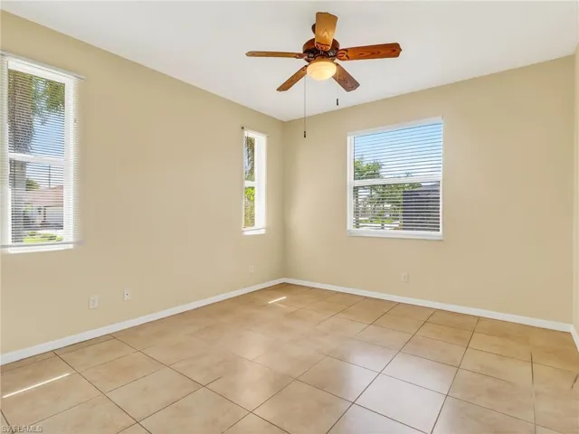 Spacious room with large ceramic tile flooring, a ceiling fan with light fixture, and multiple windows providing natural illumination