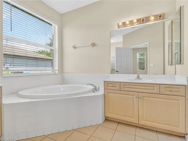 Corner soaking tub with white tiled surround and a window with blinds