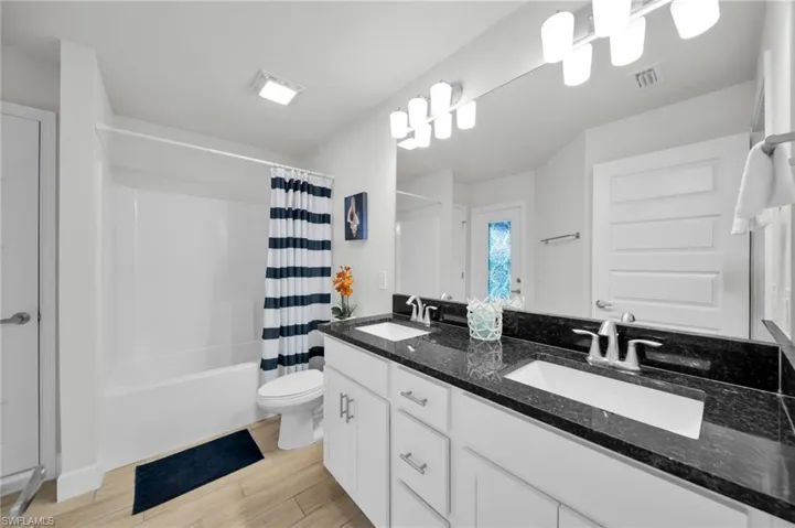 Full bathroom featuring double vanity, shower / bath combo, and light wood-style floors
