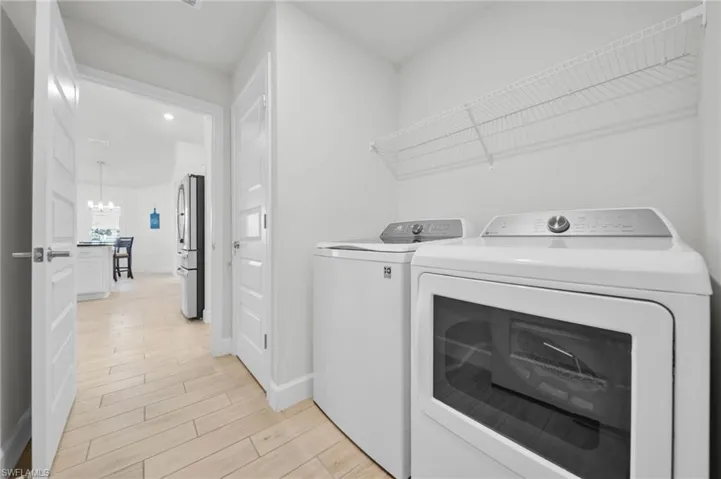 Laundry room featuring tiled wood plank floors, washer and clothes dryer, and suspended lighting