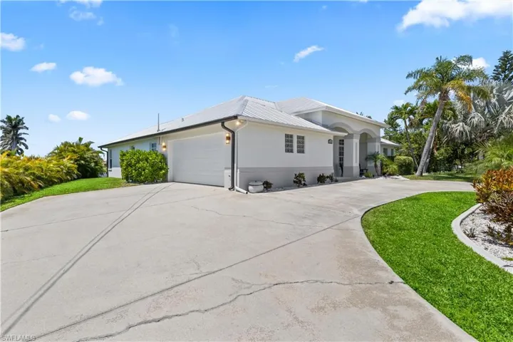 View of front facade with a front yard, metal roof, a garage, and driveway