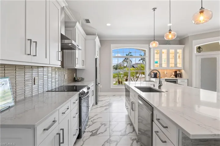 Kitchen with ornamental molding, wall chimney range hood, appliances with stainless steel finishes, marble finish floor, and a sink
