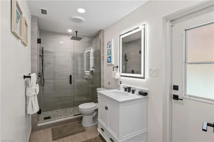Full bath featuring vanity, visible vents, toilet, wood finished floors, and a stall shower
