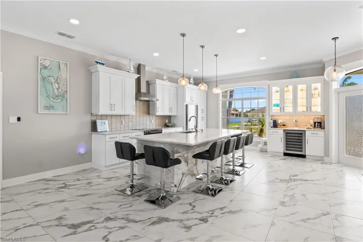 Kitchen featuring light countertops, wall chimney exhaust hood, beverage cooler, and a kitchen bar