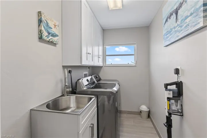 Washroom featuring baseboards, cabinet space, washer and dryer, light wood finished floors, and a sink