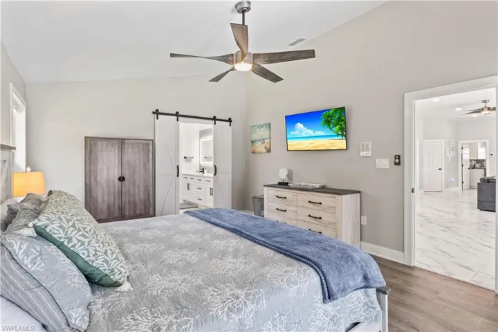 Bedroom featuring visible vents, baseboards, a barn door, ceiling fan, and vaulted ceiling