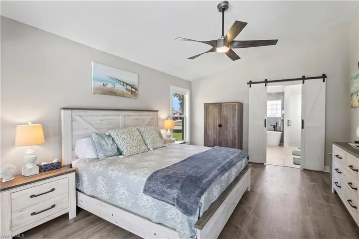 Bedroom with dark wood-style floors, ensuite bathroom, a ceiling fan, a barn door, and lofted ceiling