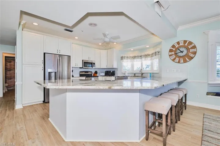 Main Kitchen with light stone counters, white cabinets, tasteful backsplash, a breakfast bar area, and a peninsula