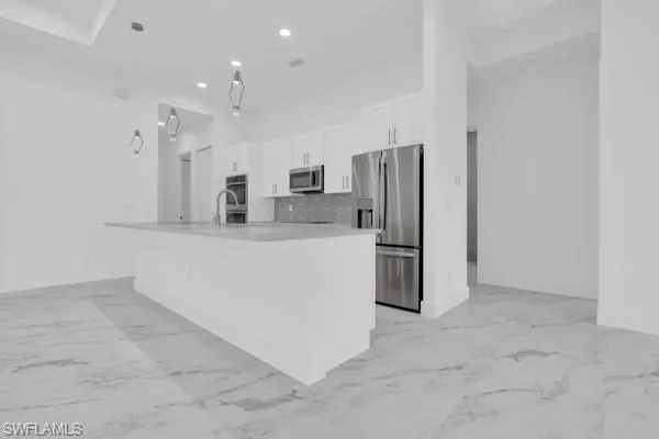 Kitchen featuring decorative light fixtures, appliances with stainless steel finishes, decorative backsplash, white cabinets, and light marble finish flooring
