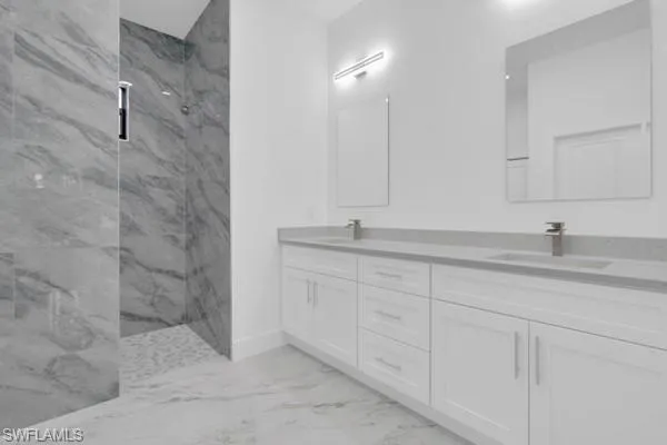 Full bath featuring a marble finish shower, double vanity, and light marble finish flooring