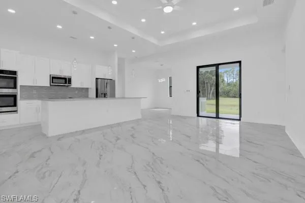 Unfurnished living room with recessed lighting, a raised ceiling, light marble finish floors, and a ceiling fan