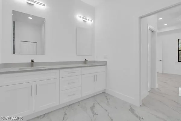 Bathroom featuring recessed lighting, double vanity, and light marble finish flooring