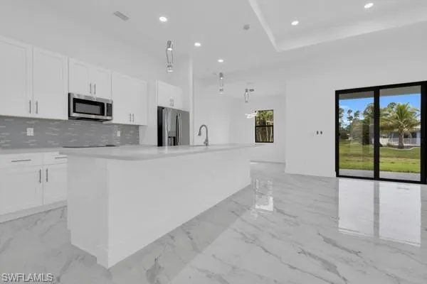 Kitchen with pendant lighting, stainless steel appliances, a kitchen island with sink, white cabinetry, and recessed lighting