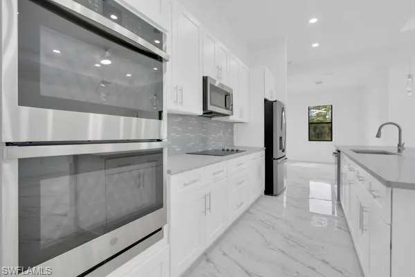 Kitchen with stainless steel appliances, light marble finish flooring, backsplash, pendant lighting, and white cabinetry