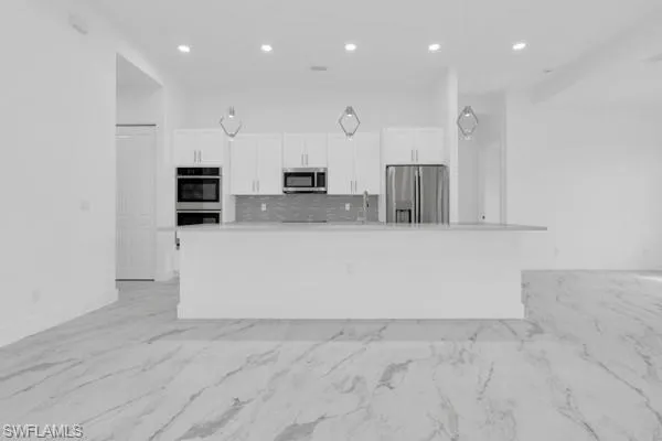 Kitchen with stainless steel appliances, tasteful backsplash, white cabinets, a large island, and recessed lighting