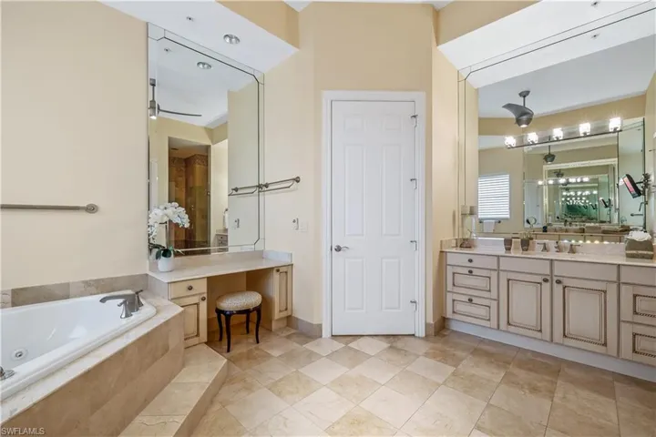 Bathroom with tiled tub, vanity, tile patterned floors, and ceiling fan