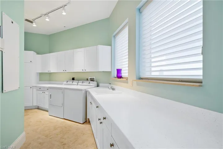 Clothes washing area featuring track lighting, sink, cabinets, light tile patterned floors, and washer and dryer