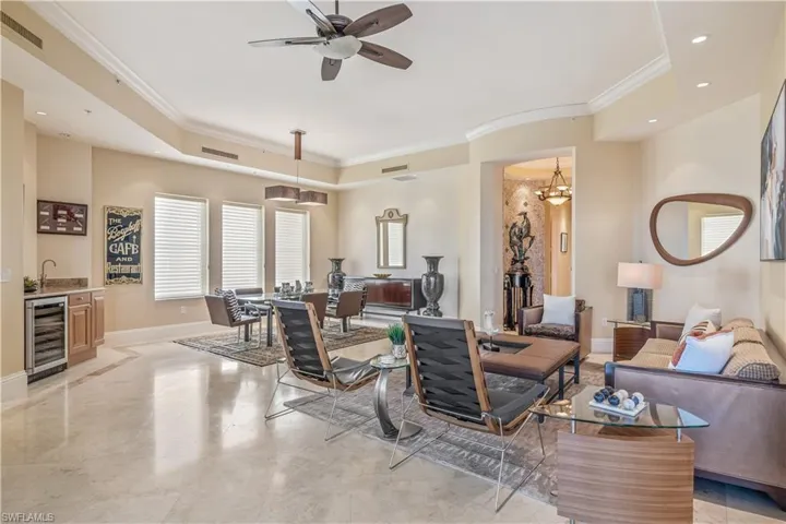 Living room featuring ceiling fan with notable chandelier, wine cooler, a raised ceiling, and ornamental molding