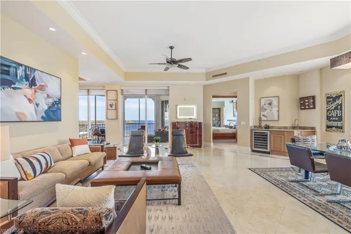 Living room featuring ceiling fan, beverage cooler, a raised ceiling, and ornamental molding