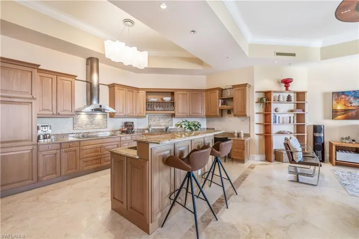Kitchen featuring a breakfast bar, light stone countertops, a raised ceiling, a center island, and wall chimney range hood