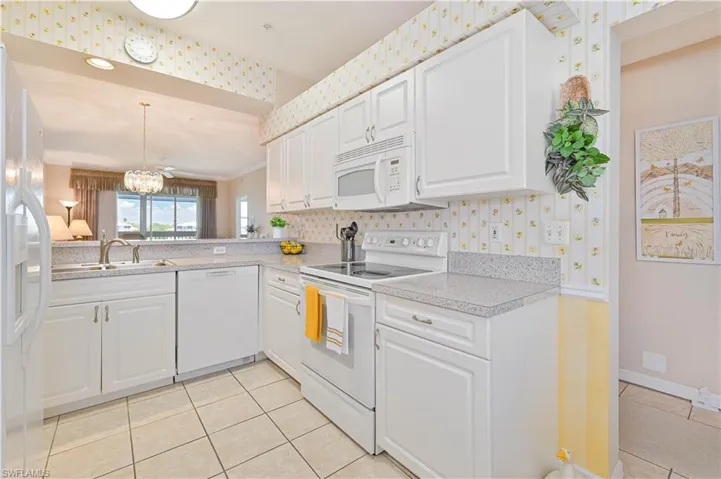 Kitchen featuring white appliances, wallpapered walls, light tile patterned floors, light countertops, and a chandelier
