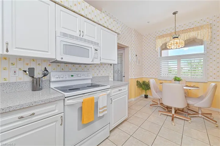 Kitchen with white appliances, wallpapered walls, white cabinets, hanging light fixtures, and baseboards