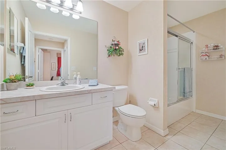 Bathroom featuring tile patterned flooring, toilet, vanity, and bath / shower combo with glass door