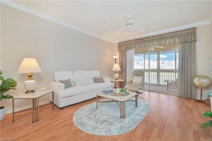 Living room featuring ornamental molding, a ceiling fan, light wood finished floors, a water view, and baseboards