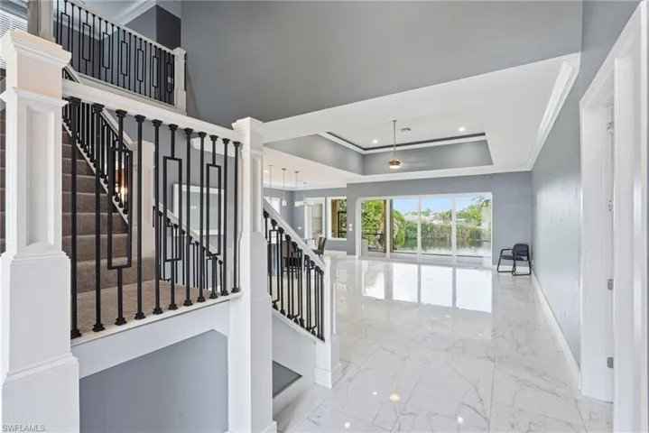 Staircase with marble tiled floors, ornamental molding, recessed lighting, a raised ceiling, and decorative columns