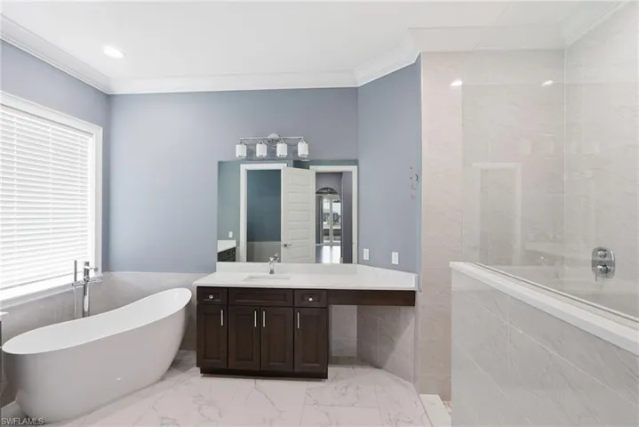 Full bathroom featuring a freestanding bath, vanity, ornamental molding, a walk in shower, and light marble finish floors