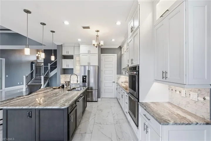 Kitchen featuring decorative backsplash, a chandelier, white cabinetry, pendant lighting, and stainless steel appliances