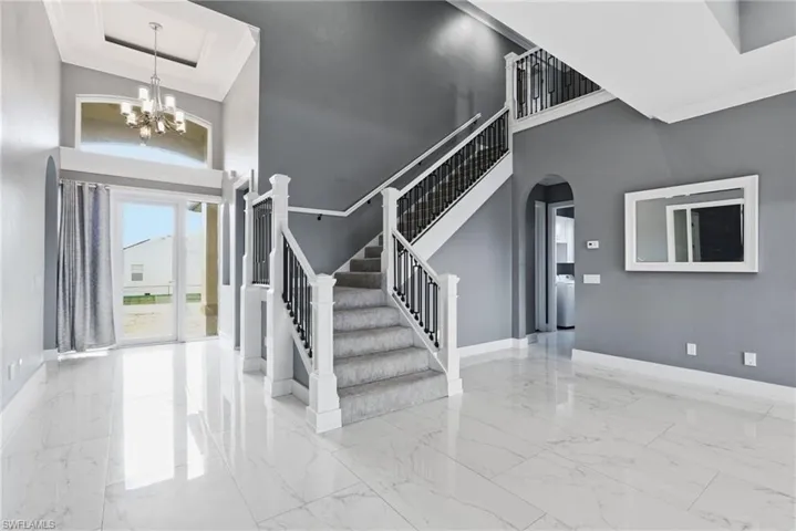 Entrance foyer with crown molding, a high ceiling, arched walkways, stairway, and a chandelier