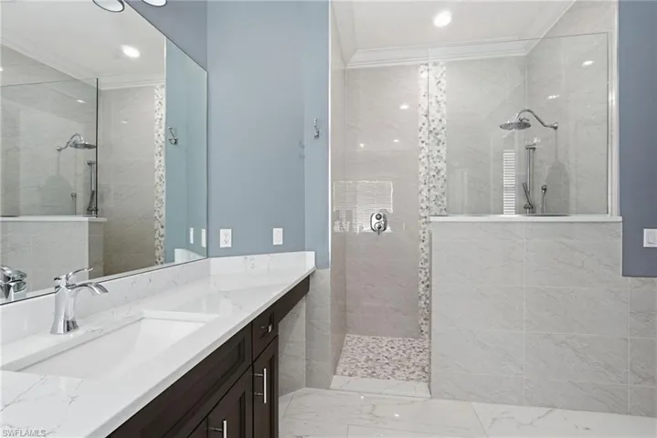 Bathroom featuring a walk in shower, vanity, light marble finish floors, crown molding, and recessed lighting