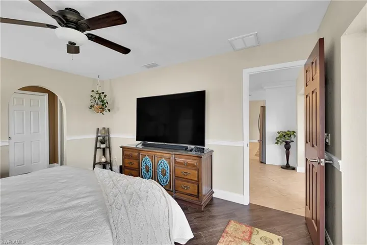 Bedroom with dark wood-style flooring, ceiling fan, arched walkways, and freestanding refrigerator