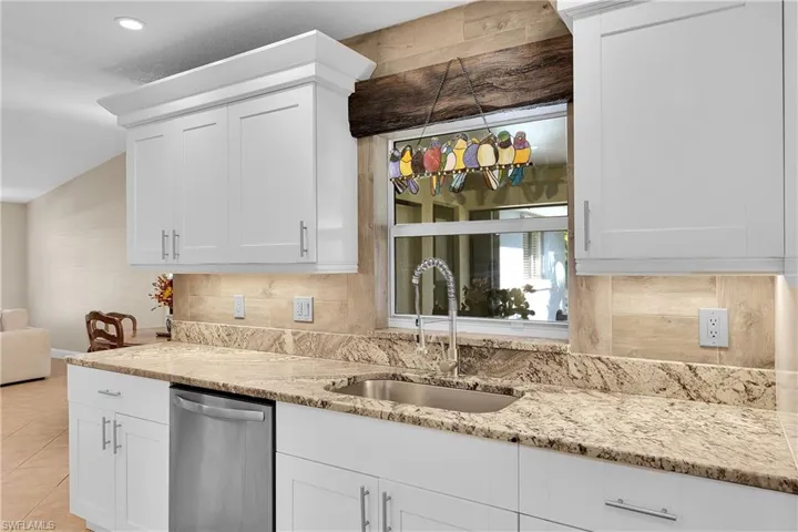 Kitchen featuring stainless steel dishwasher, light stone countertops, white cabinets, and backsplash