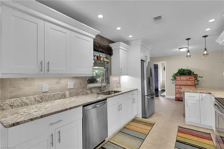 Kitchen with decorative light fixtures, white cabinetry, backsplash, stainless steel appliances, and light stone counters