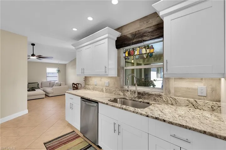 Kitchen featuring stainless steel dishwasher, backsplash, light stone counters, recessed lighting, and white cabinets