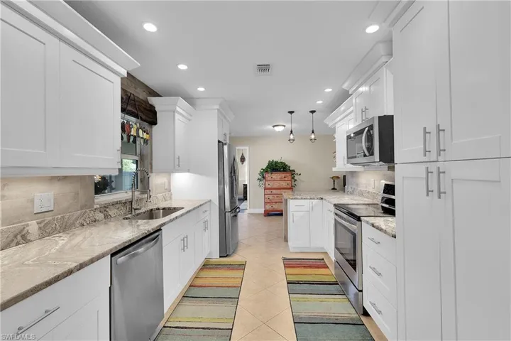 Kitchen featuring stainless steel appliances, pendant lighting, backsplash, white cabinets, and light stone countertops