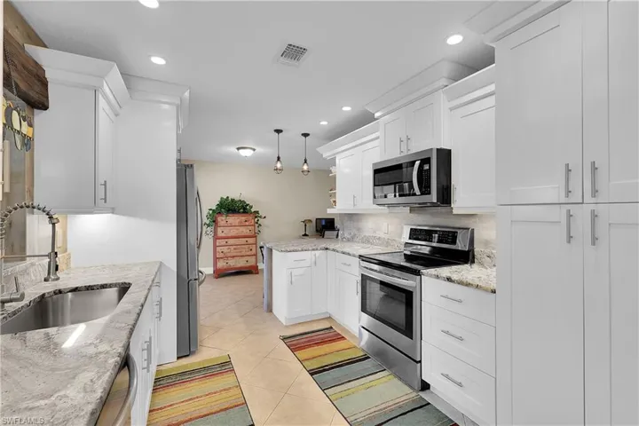 Kitchen featuring stainless steel appliances, white cabinets, hanging light fixtures, light stone counters, and recessed lighting
