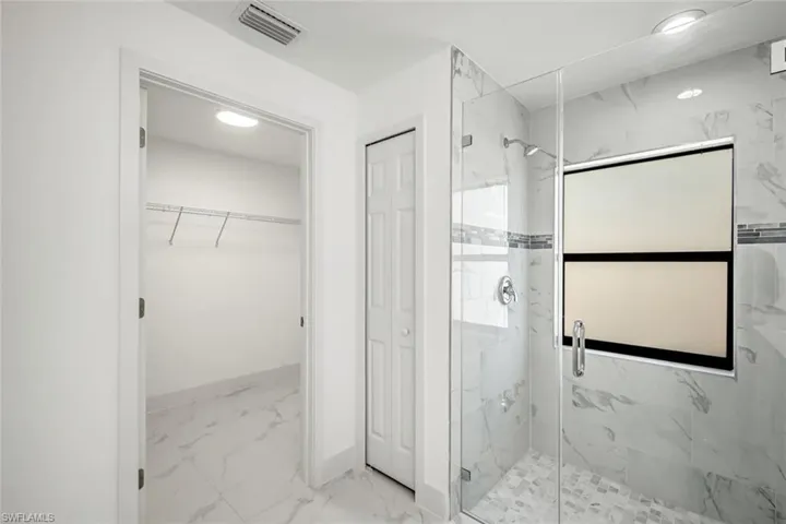 Spacious primary bathroom featuring light marble finish flooring, a marble finish shower, a walk in closet, and recessed lighting.