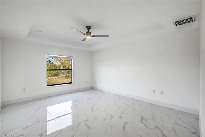 Spacious bedroom featuring a raised/tray-style ceiling, ceiling fan, and bright neutral finishes for a calm retreat.