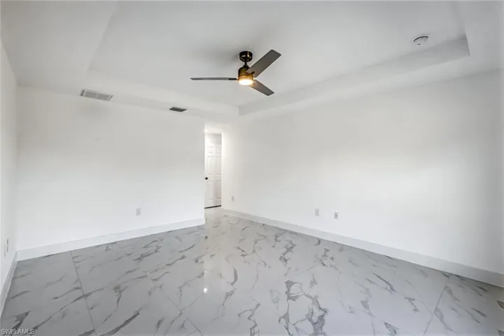 Spacious bedroom featuring a raised/tray-style ceiling, ceiling fan, and bright neutral finishes for a calm retreat.