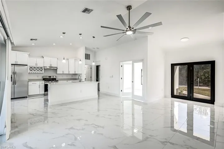 Airy open layout connecting living and kitchen spaces, featuring oversized tile flooring and multiple windows/doors for a bright feel.