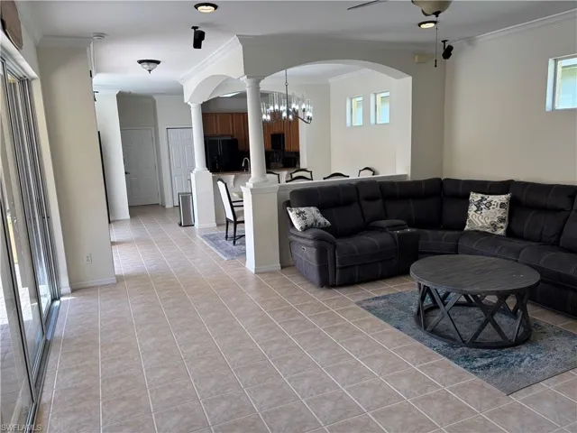 Living room featuring ornamental molding, a chandelier, light tile patterned floors, and arched walkways