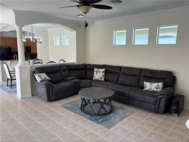 Living area with crown molding, ceiling fan, light tile patterned floors, a chandelier, and arched walkways