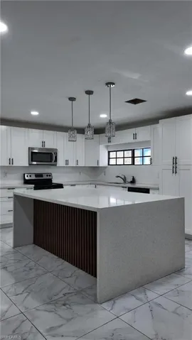 Kitchen with a spacious island, light stone counters, stainless steel appliances, decorative light fixtures, and white cabinetry