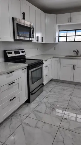 Kitchen with stainless steel appliances, white cabinets, light stone counters, and light marble finish floors