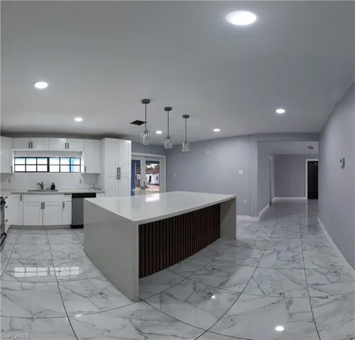 Kitchen featuring a center island, light stone counters, stainless steel dishwasher, hanging light fixtures, and white cabinetry