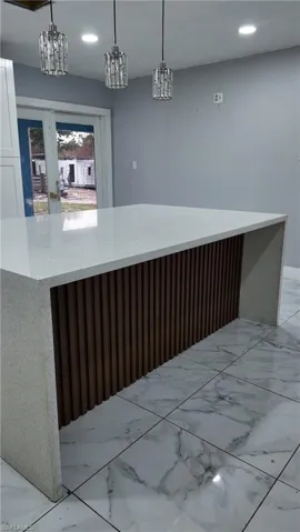 Bar with light stone countertops, light marble finish flooring, and decorative light fixtures