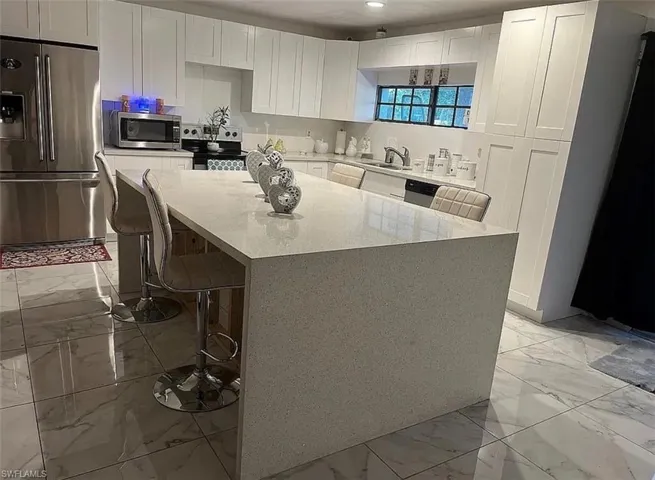Kitchen with stainless steel appliances, a kitchen bar, light stone counters, and white cabinetry